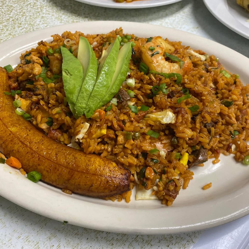 A plate of arroz chaufa with shrimp, chicken, avocado slices, and a fried plantain.