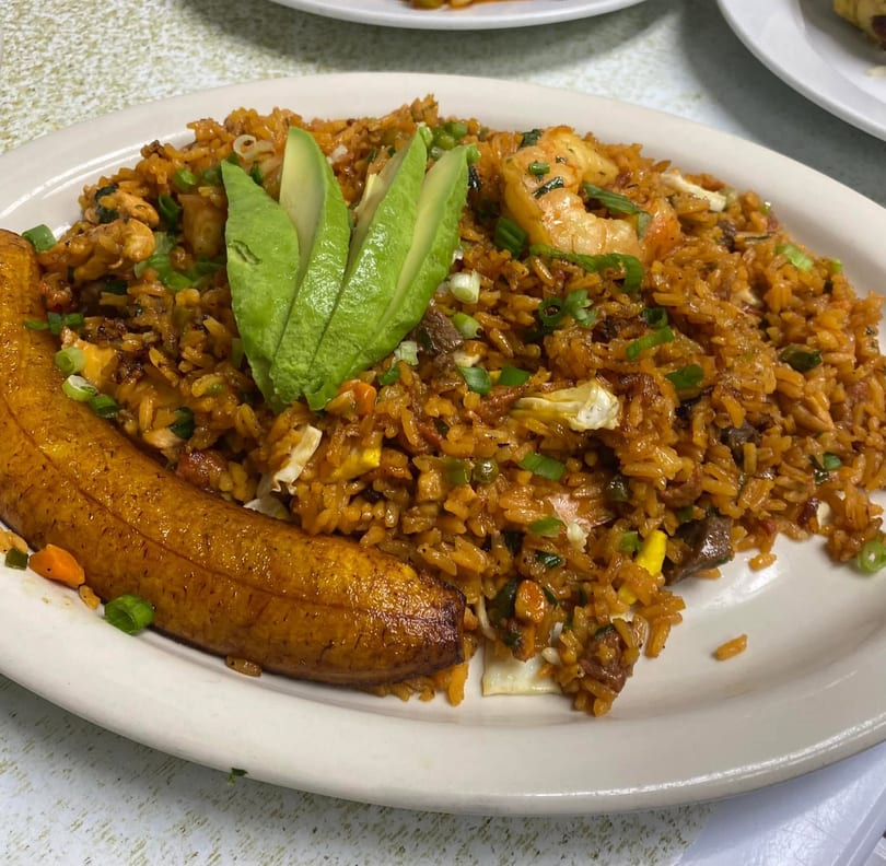 A plate of arroz chaufa with shrimp, chicken, avocado slices, and a fried plantain.